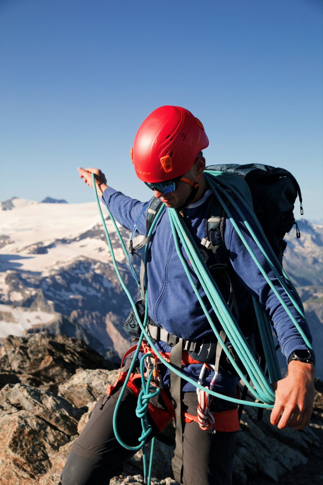 A mountaineer in a red helmet coiling a climbing rope on a summit ridge