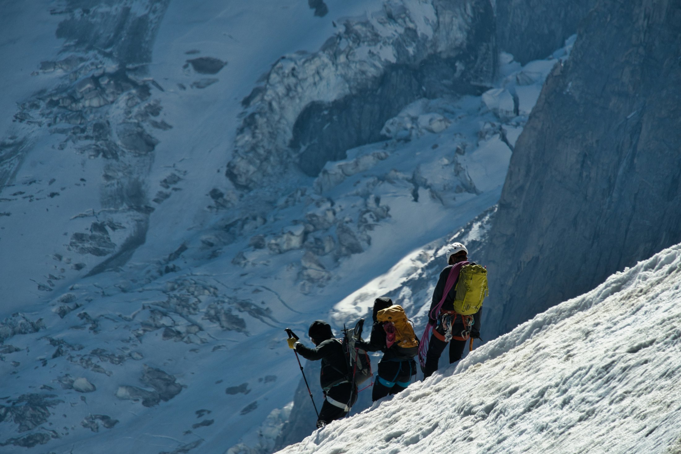 Three roped mountaineers climbing a steep snow slope above a glacier